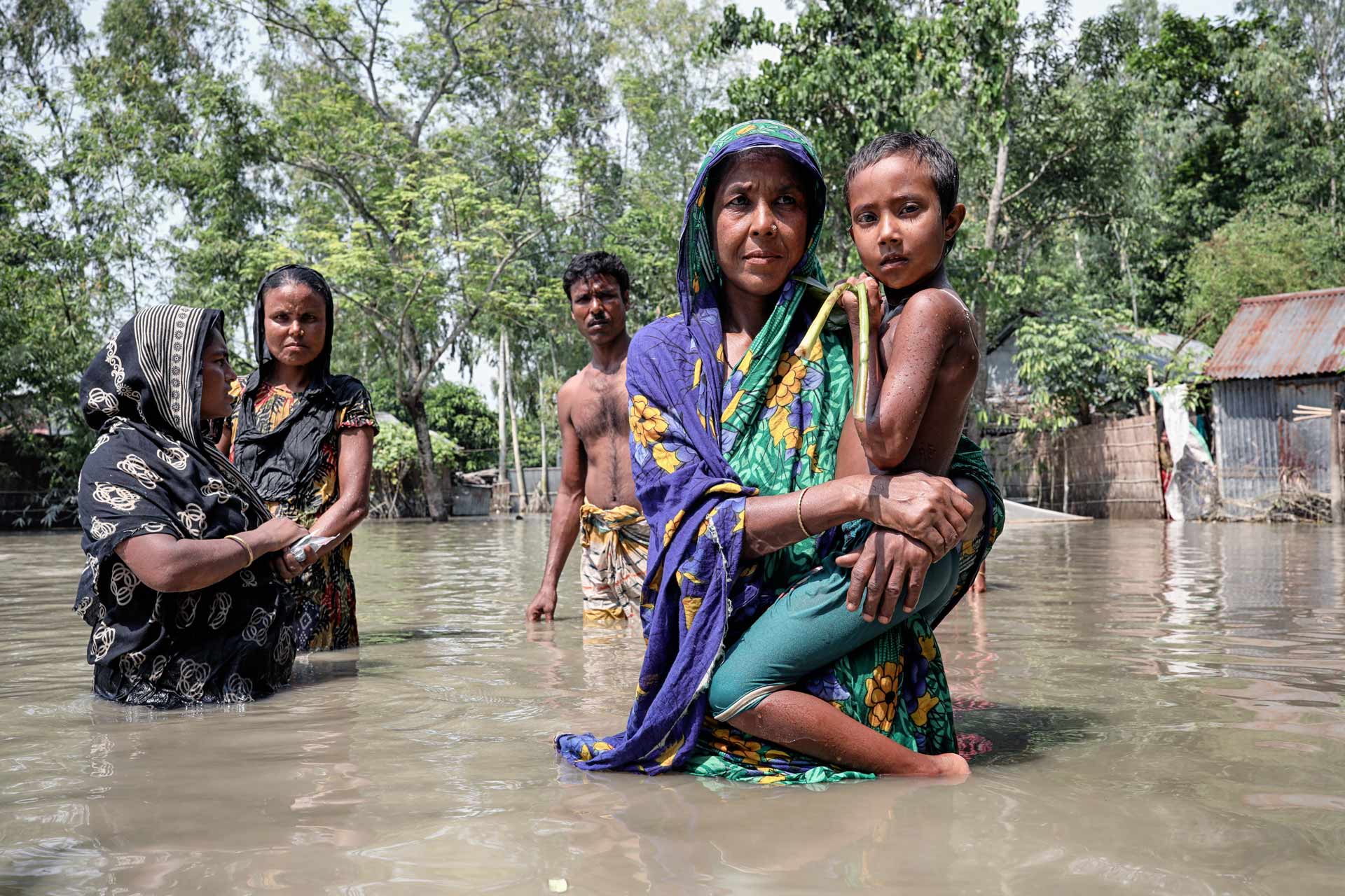A group of people standing in flood waters. A woman is holding a child.